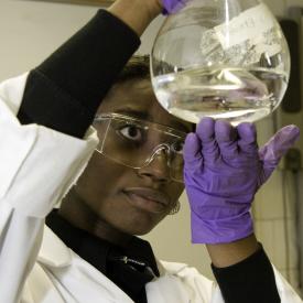 female student in lab coat examining beaker science