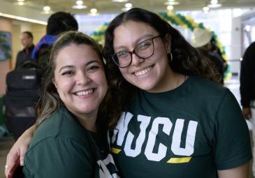 two female students pose, hug, smile