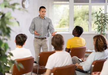 man stands at front of classroom with seated students