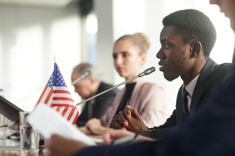 SEATED MAN WITH MIC AND AMERICAN FLAG