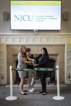 ribbon cutting event, 2 women, 1 boy, screen above